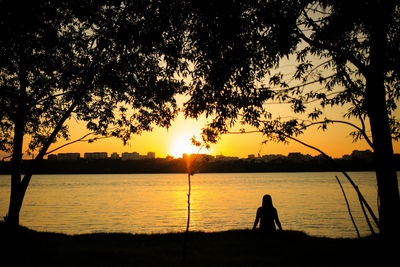 Silhouette person standing by lake against sky during sunset