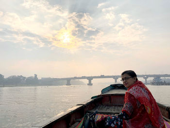 Woman sitting on boat in river against sky during sunset