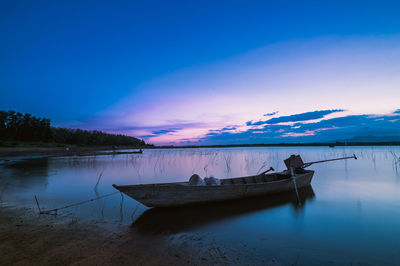 Boat moored in lake against sky at sunset