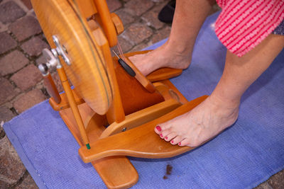 Traditional wooden spinning wheel, woman spinning wool, bare feet on pedal, outdoor setup, craftwork