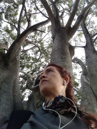 Low angle portrait of woman against tree trunk