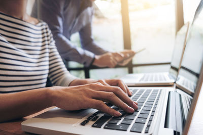 Midsection of colleagues using laptop at desk in office