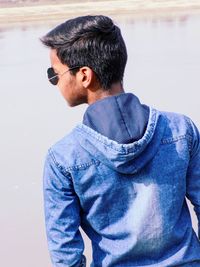 Young man looking away while standing against blue wall