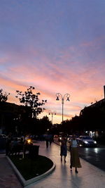 Silhouette people on street against sky at sunset