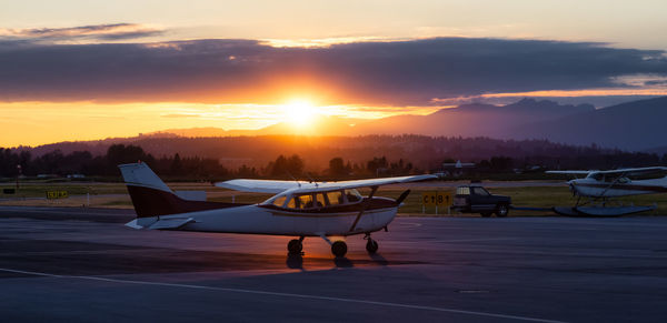 Airplane on airport runway against sky during sunset