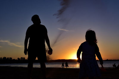 Silhouette people on beach against sky during sunset