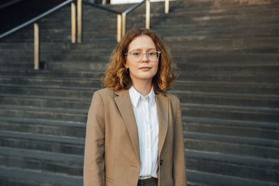 Young beautiful redhead businesswoman standing in front of staircase