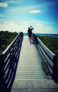 Man walking on footbridge against sky