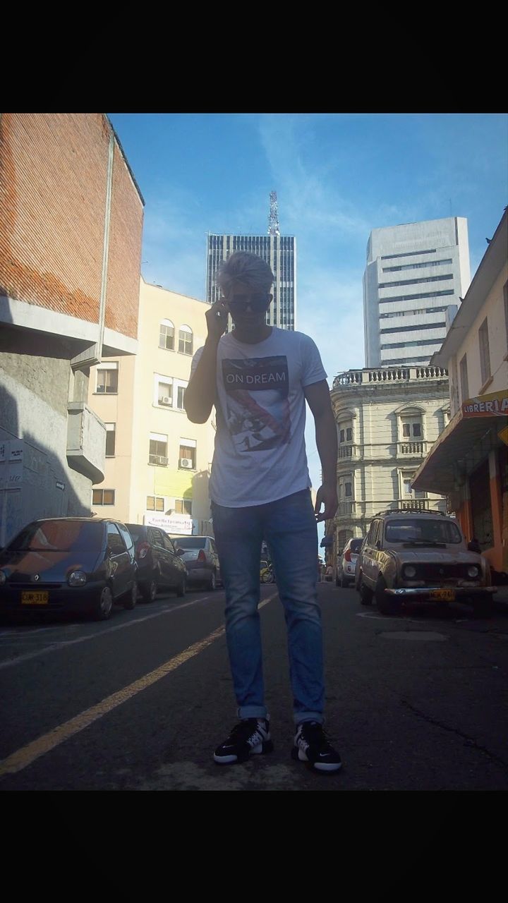 MAN STANDING ON ROAD AGAINST CITYSCAPE