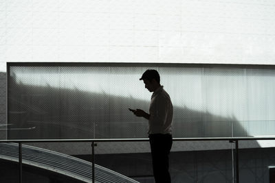 Side view of man using mobile phone against wall