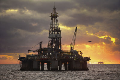 Oil rigs in sea against cloudy sky sunset