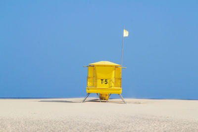 Lifeguard hut on beach against clear blue sky with flag raised seems a lander