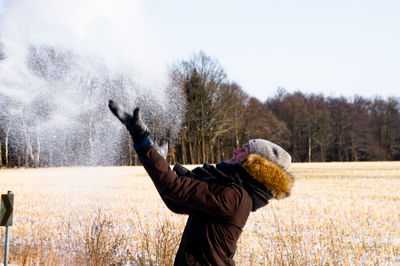 Woman playing with snow on field against sky