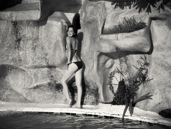 Smiling beautiful woman in bikini standing at poolside against rock