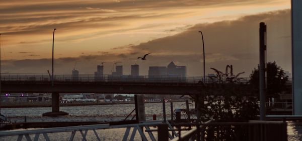 Bridge over river by buildings against sky during sunset