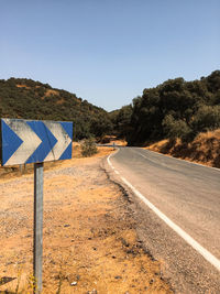 Road sign by trees against clear sky