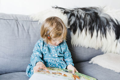 Cute girl holding picture book sitting on sofa at home