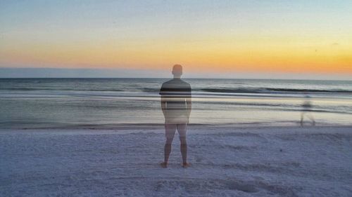 Rear view of man standing on beach during sunset