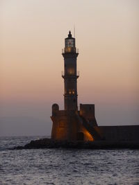 Low angle view of lighthouse by sea against clear sky at dusk