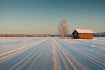 Frozen house on snowy landscape against clear sky during winter