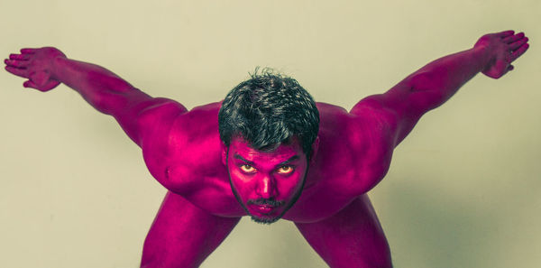 Portrait of naked man in magenta paint against colored background