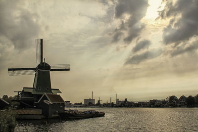 Traditional windmill by river against sky