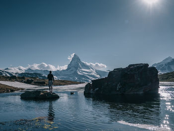 Rear view of man standing by lake during winter on sunny day