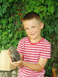 Portrait of smiling boy holding owl against plants