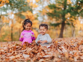 Cute siblings playing while sitting on autumn leaf in forest