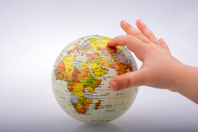 Close-up of hand holding globe against white background