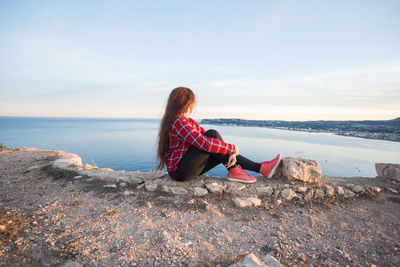 Woman sitting on rock by sea against sky