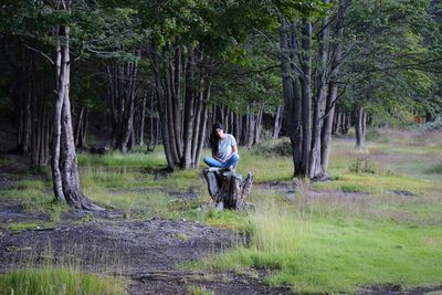 Woman sitting against trees at forest