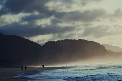 Silhouette people on beach against sky during sunset