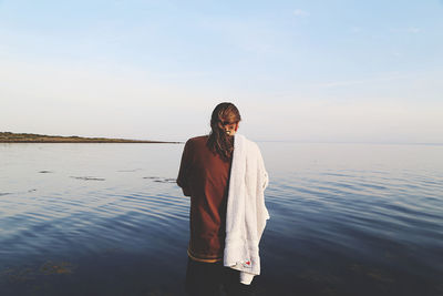 Rear view of man standing with towel by sea against sky