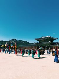 Group of people wearing traditional clothing in town against clear blue sky during sunny day