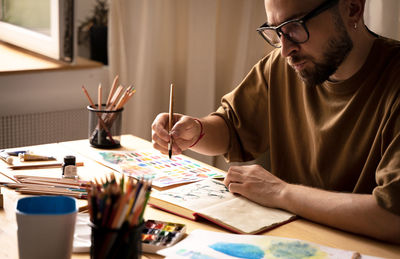 Male artist drawing, sketching. color pencils in a hand. craftmen sitting on table