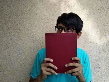 Thoughtful man holding book while standing against wall