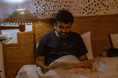 Full length of young man sitting on bed at home