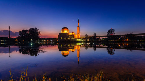 Reflection of illuminated buildings in lake against sky during sunset