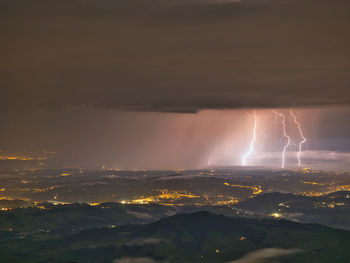 Aerial view of illuminated cityscape against dramatic sky and lightning 
