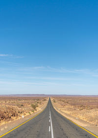 Empty road against clear blue sky