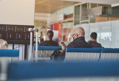 Senior man with smartphone charging devices in airport lounge with luggage hand-cart. 