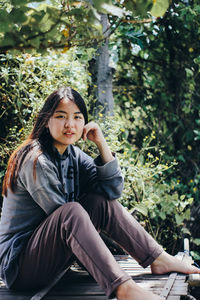 Portrait of smiling young woman sitting against trees