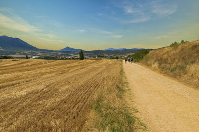 Dirt road amidst field against sky