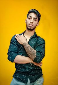 Portrait of young man standing against yellow wall