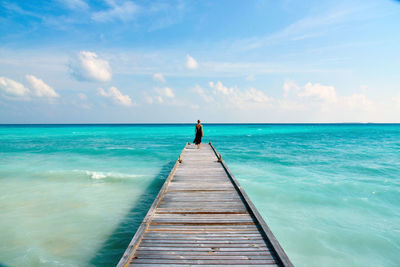 Rear view of woman walking on pier over sea against sky