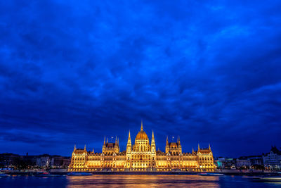 Illuminated hungarian parliament building and danube river in city at dusk