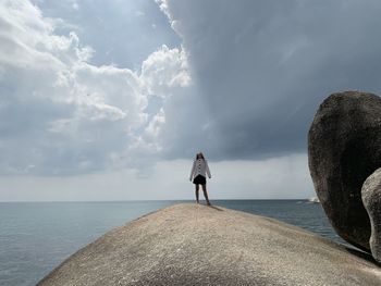 Rear view of man standing on rock by sea against sky