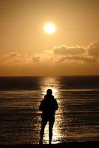 Silhouette woman standing at beach against sky during sunset