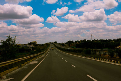 Road passing through landscape against cloudy sky